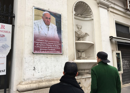 Ein papstkritisches Plakat an einer Wand in Rom am 5. Februar 2017. Zwei Passanten stehen davor und betrachten das Plakat. Unter dem Foto von Papst Franziskus steht in römischem Dialekt: 'Franziskus, du hast Kongregationen unter kommissarische Leitun